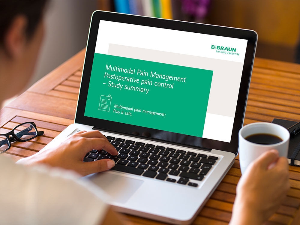 Auf einem Tisch steht ein Laptop, davor sitzt eine Frau. Sie hält einen CoNee-Becher in ihrer rechten Hand und ihre linke Hand ruht auf der Tastatur. Auf dem Bildschirm stehen „Multimodales Schmerzmanagement Postoperative Schmerzkontrolle – Studienzusammenfassung“ und "Multimodales Schmerzmanagement: Auf Nummer sicher gehen."