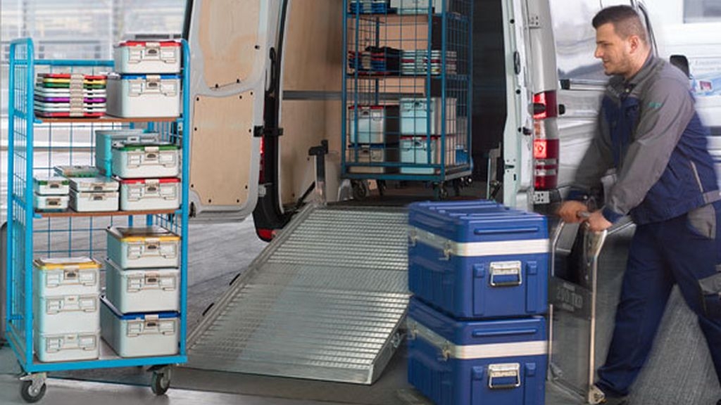 Das Bild zeigt einen Mitarbeiter des technischen Kundendienstes von B. Braun, der einen Wagen mit Kisten voller Produkte schiebt, die an den Kunden geliefert werden.
