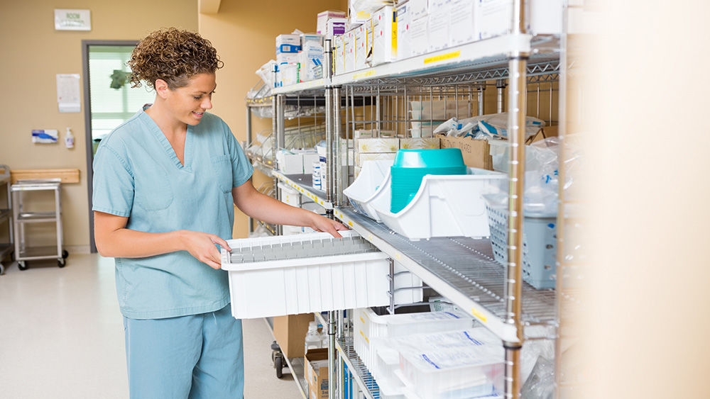 Mid adult female nurse arranging container on shelf in hospital storage room