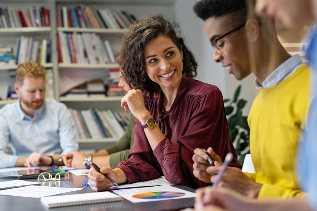 Eine Gruppe von jungen Studierenden sitzen zusammen an einem Konferenztisch und freuen sich über die Zusammenarbeit