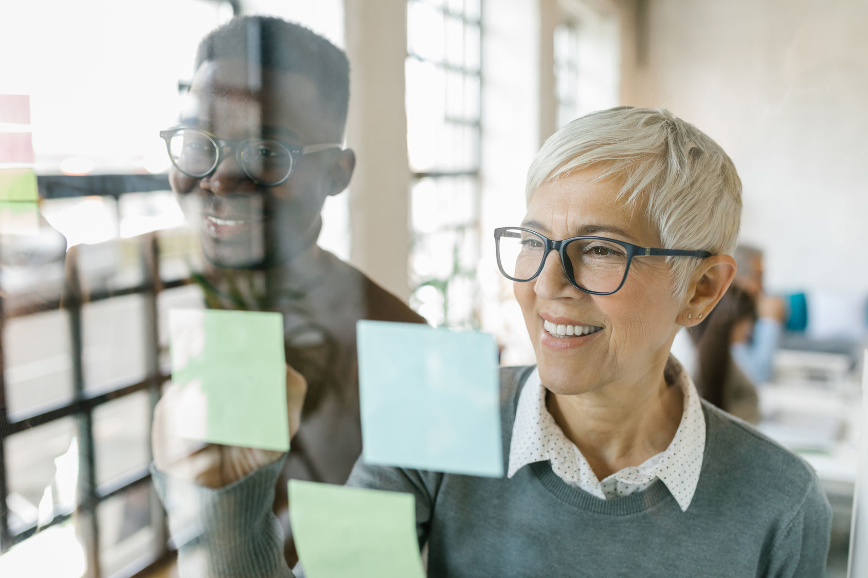 Colleagues writing notes on a stickers on a glass wall