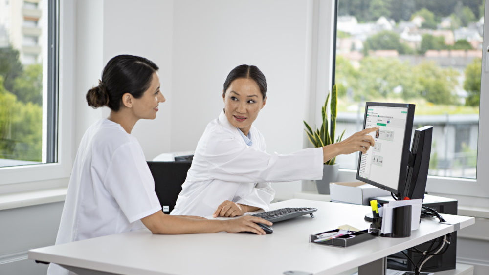 Eine weibliche medizinische Fachkraft nutzt NEXADIA® auf dem Monitor und zeigt ihrer Kollegin etwas