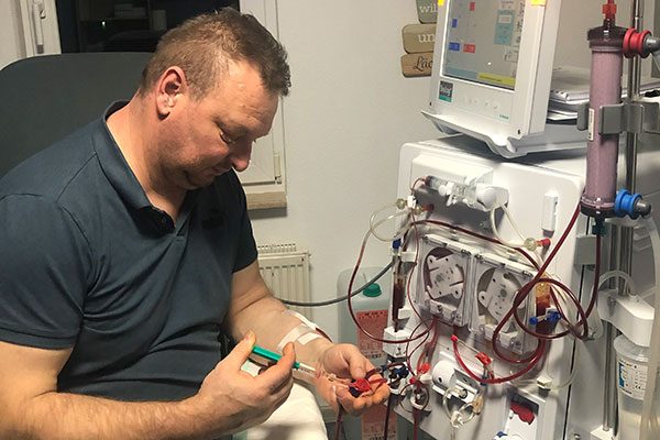 Jens sitzt vor dem Dialysegerät und nimmt Einstellungen an dem Gerät vor. 