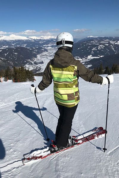 Nicol Wahl ist von hinten zu sehen, sie steht auf Skiern auf einer Piste und blickt hinunter ins Tal.  