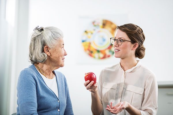 Eine Patientin befindet sich im Gespräch mit ihrer Ernährungsberaterin, die einen Apfel in der Hand hält.