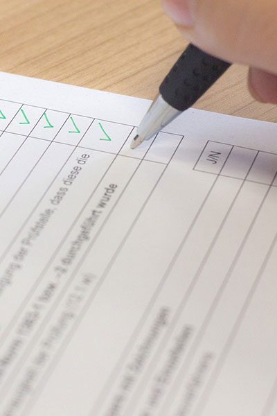Detailaufnahme einer Checkliste, die mit einem Kugelschreiber abgehakt wird. 