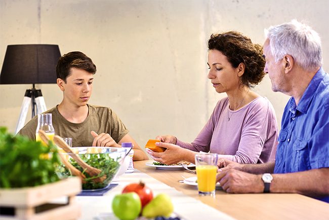 Familie sitzt gemeinsam am Tisch und isst frischen Salat und gesunde Lebensmittel