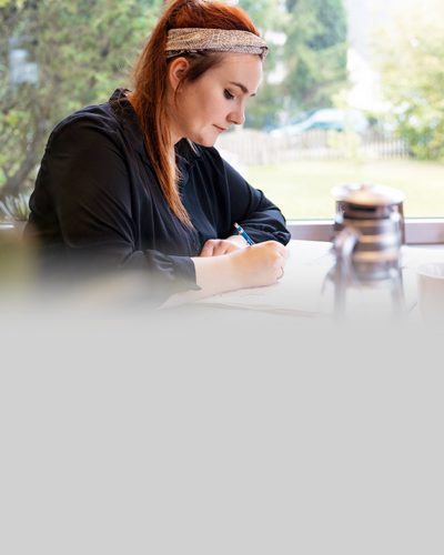 Eine junge Frau mit Stoma sitzt an ihrem Schreibtisch und zeichnet.