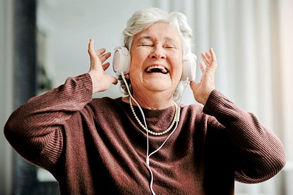 Eine ältere Frau hat Kopfhörer auf und lacht herzlich.