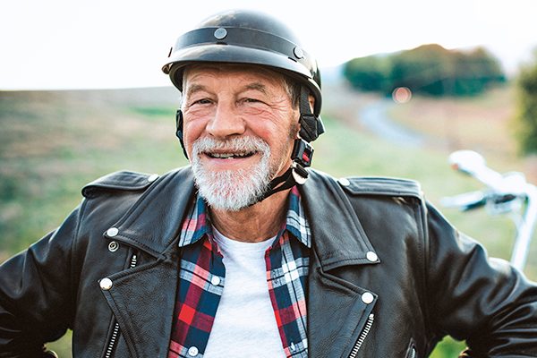 Ein älterer Mann sitzt auf dem Motorrad und lächelt in die Kamera. 