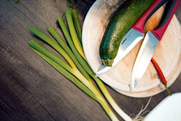 Zucchini, Chilli und Lauch liegen auf einem Schneidebrett neben zwei Messern. 