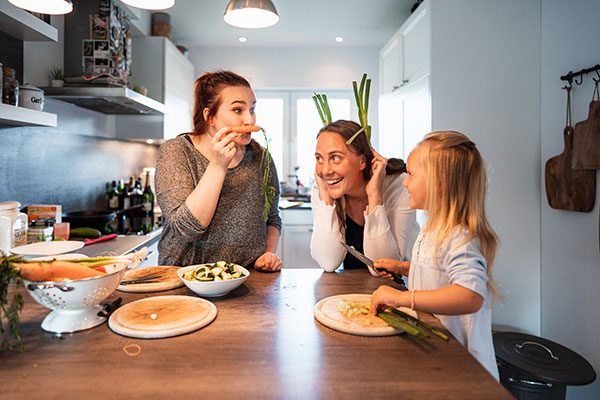 Zwei Frauen und ein Kind stehen lachend in der Küche und kochen. 