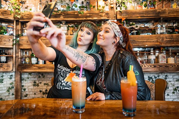 Zwei junge Frauen sitzen in einer Bar und machen zusammen ein Selfie. 