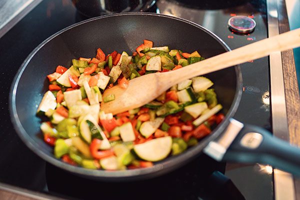 In einer Pfanne befindet sich Gemüse und ein Kochlöffel. 