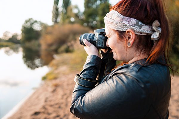 Eine junge Frau mit Stoma geht ihrem Hobby nach und fotografiert mit einer Spiegelreflexkamera die Landschaft.