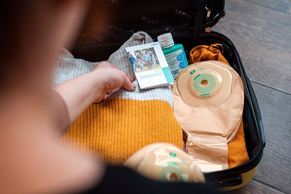 Eine Frau packt ihren Koffer für den Urlaub mit Stoma. Im Koffer befinden sich ein Stoma-Pass sowie Versorgungsmaterialien.