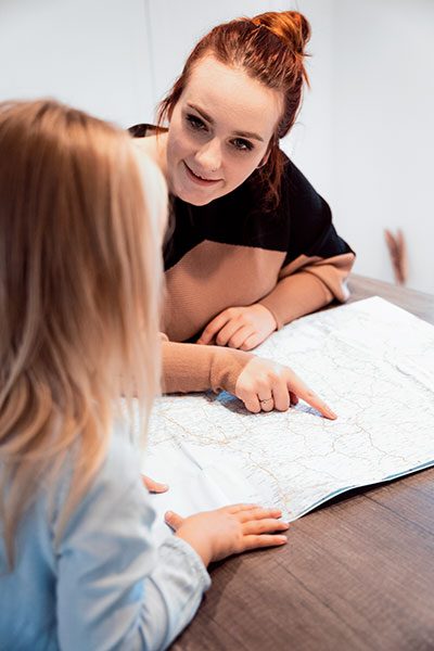 Eine junge Frau zeigt ihrem Kind etwas auf einer Landkarte. 