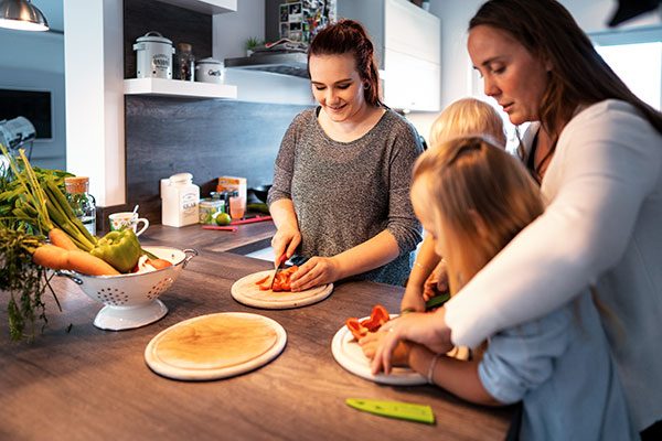 Zwei Frauen und zwei Kinder schneiden gemeinsam Gemüse in einer Küche. 