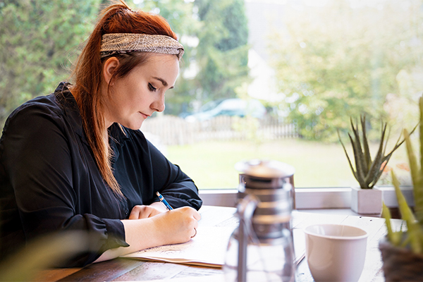 Eine Frau sitzt an einem Tisch und schreibt in ein Tagebuch.