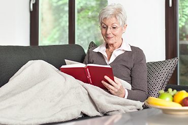 Eine Patientin sitzt während der Bauchfelldialyse auf dem Sofa und liest ein Buch.