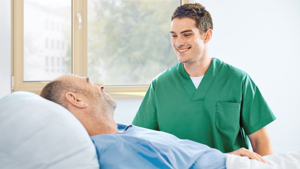 Eine Pflegekraft spricht mit einem Patienten am Bett
