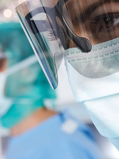 Ärztin trägt Maske und Spezialbrille, sieht besorgt aus, während sie einen Eingriff beobachtet