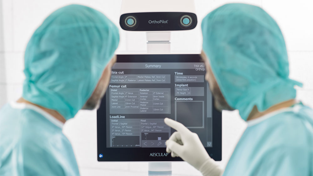 Zwei Ärzte mit Kitteln und Handschuhen schauen auf den Orthopilot Elite, ein Arzt zeigt auf den Bildschirm.