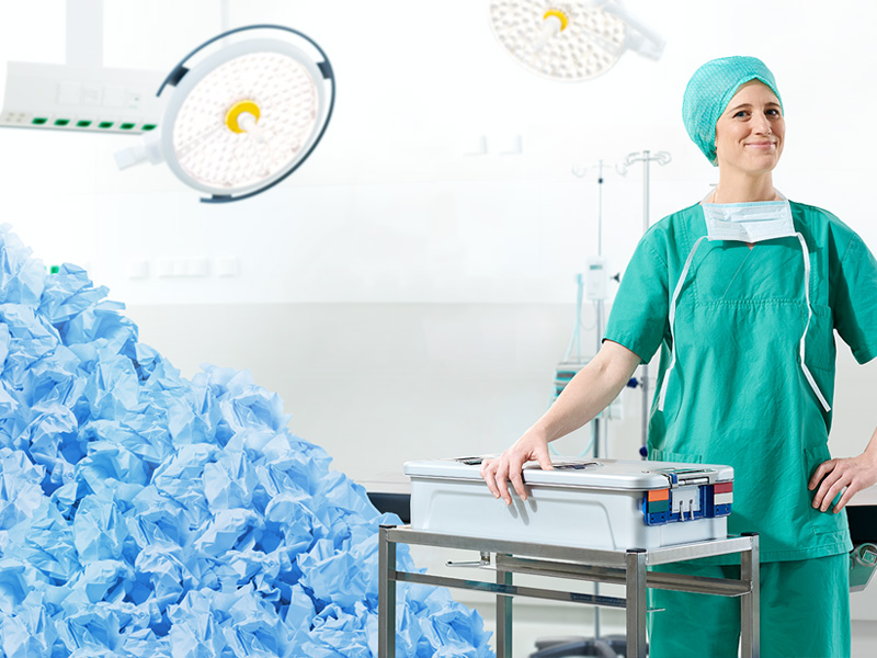Eine medizinische Fachkraft steht hinter einem Tisch mit einem großen Stapel gebrauchter medizinischer Kleidung im Hintergrund