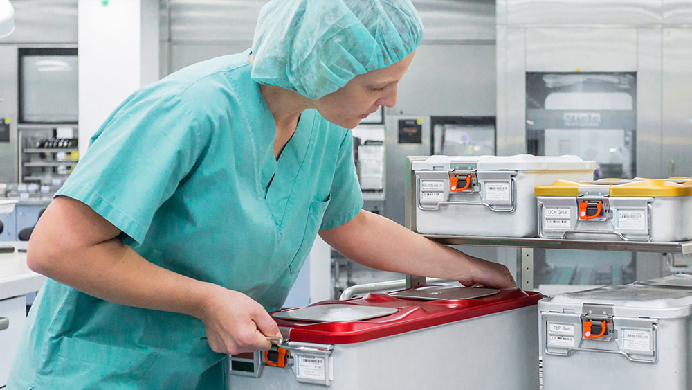 Eine medizinische Fachkraft stellt einen großen Behälter auf ein Lagerregal in einem medizinischen Versorgungsraum