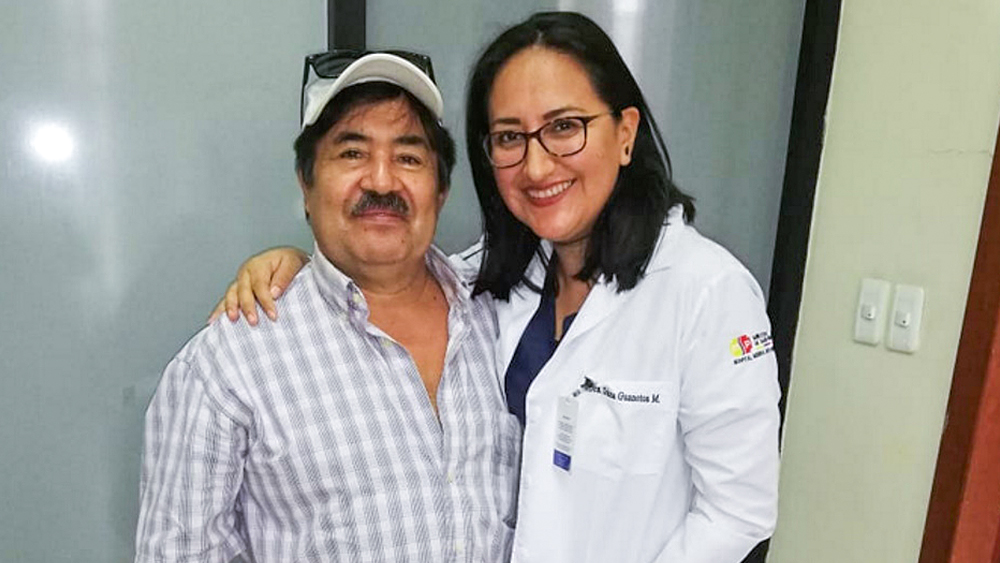 Mann und Frau stehen nebeneinander und lächeln. Die Frau hält ihren Arm um den Mann