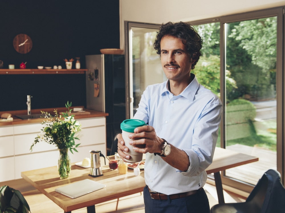 Ein Mann steht in einem Privathaus und hält eine Tasse Kaffee
