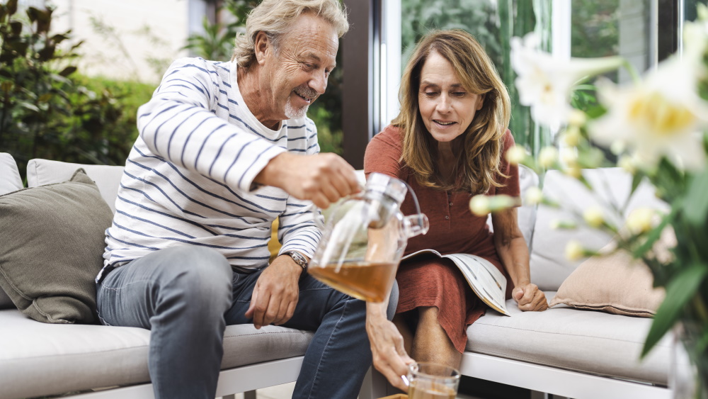 Ein mittelalterlicher Mann und eine Frau sitzen zusammen auf dem Sofa und der Mann gießt der Frau eine Tasse Tee ein